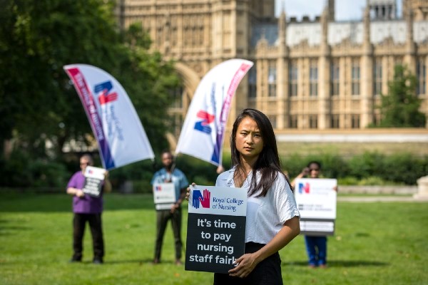 A nurse outside parliament in London, holding a placard for fair pay for nurses